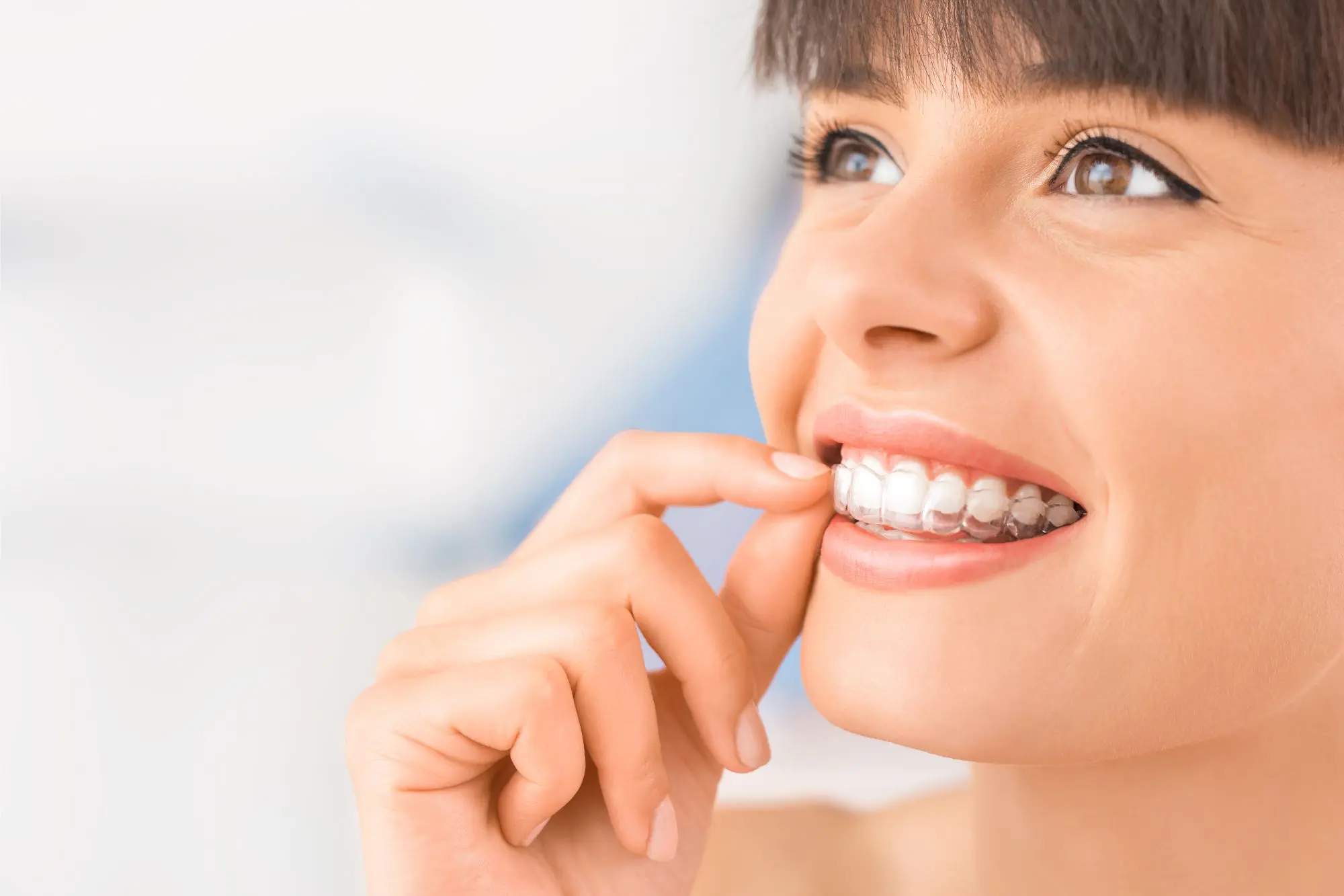 A person smiling while adjusting a Invisalign from NK Orthodontics in their mouth in Suwanee, GA.