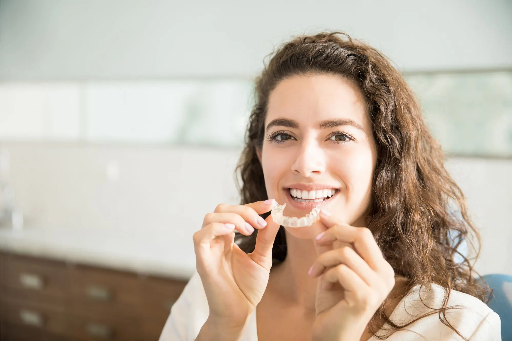 A woman smiles brightly, showcasing her clear dental aligner in front of her teeth, a testament to the expert care at NK Orthodontics in Tucker, GA