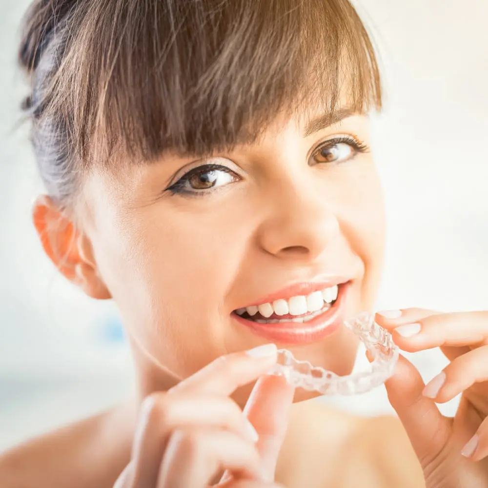A person smiling holds a clear dental aligner close to their mouth, showcasing the effective treatment offered by NK Orthodontics in Suwanee, GA.