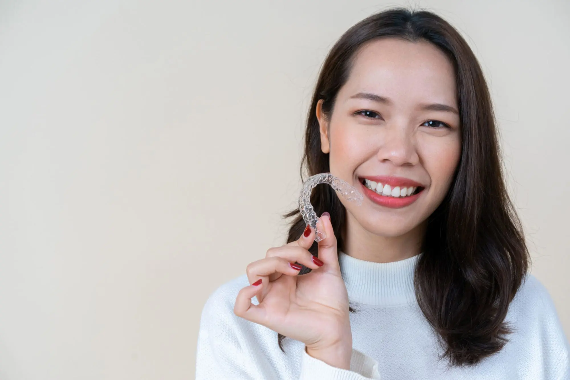 A person from NK Orthodontics smiles while holding a clear dental aligner in Suwanee, GA.