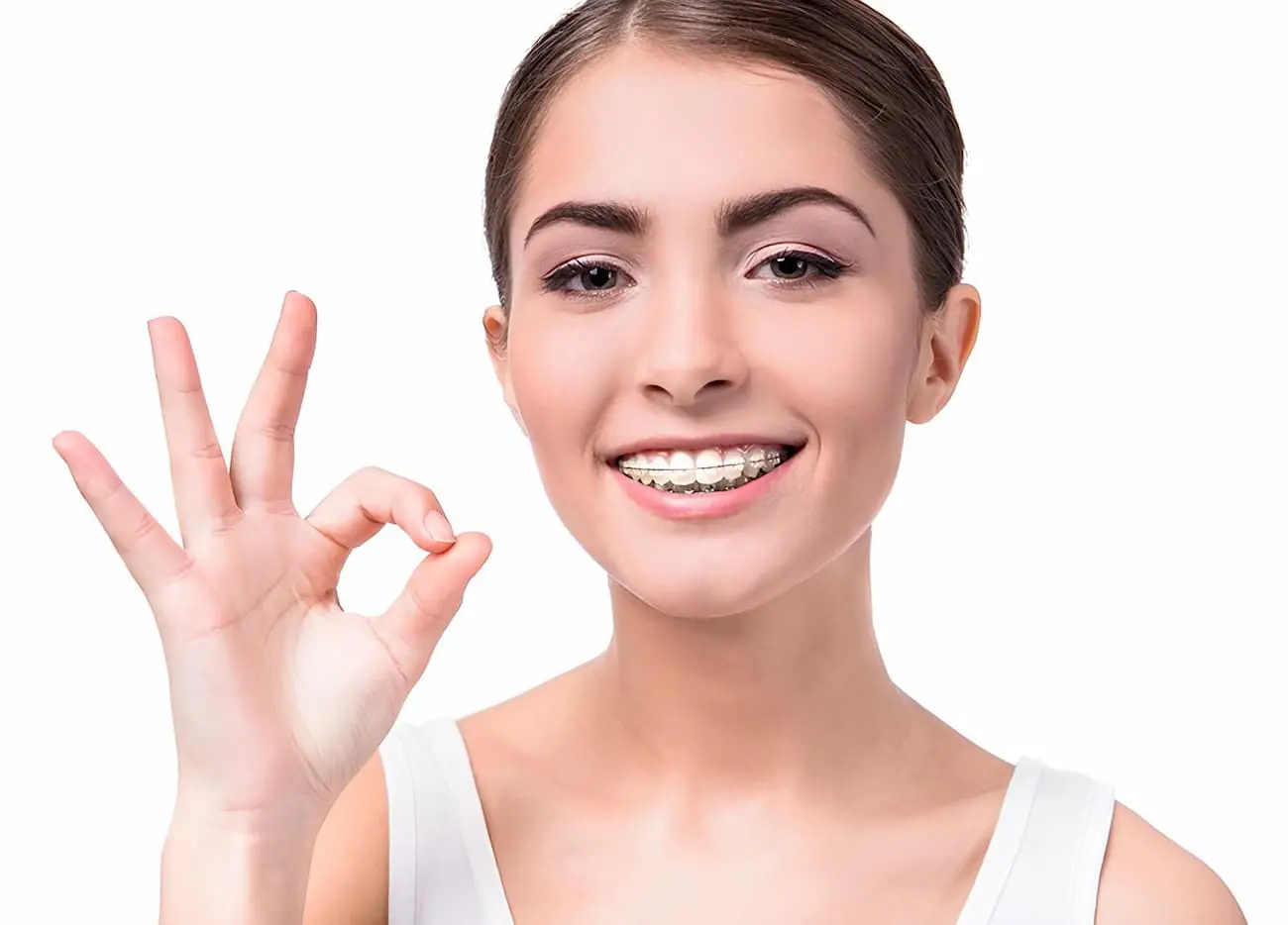 A person with NK Orthodontics clear braces smiles and gestures the "OK" sign with their hand against a white background in Suwanee or Tucker, GA