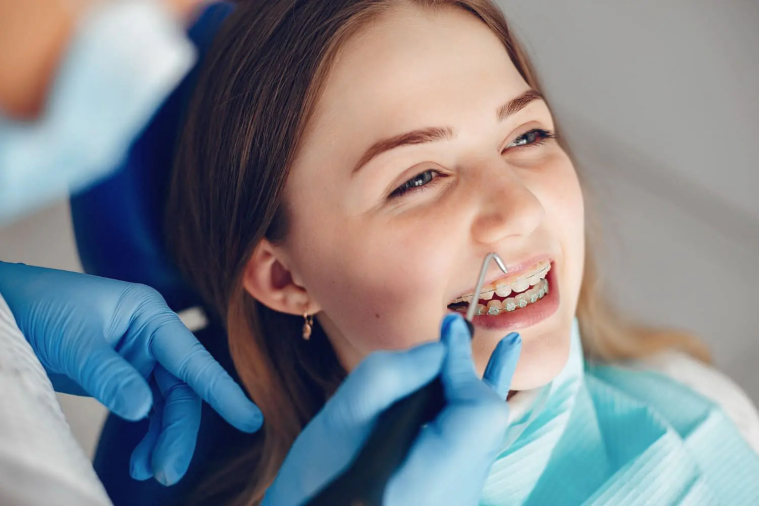 A dental professional wearing gloves carefully adjusts clear braces on a young person in the dental chair in Tucker, GA