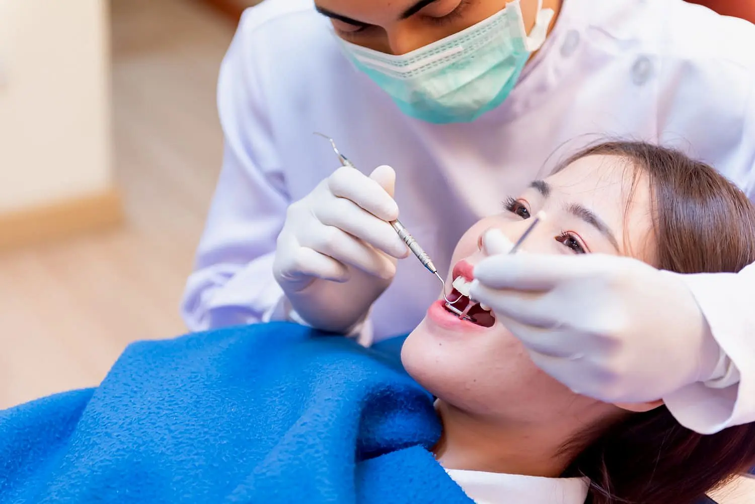 The dentist examines a patient's teeth, using dental tools expertly while the patient, relaxed under a blue blanket, reclines. The dentist, wearing a mask and gloves, also discusses orthodontic appliances to enhance the patient's dental care plan in Tucker, GA