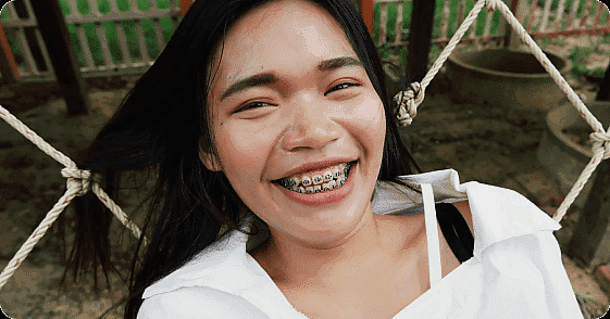 A person with long dark hair and braces is smiling enjoying the warm weather in Suwanee or Tucker, GA