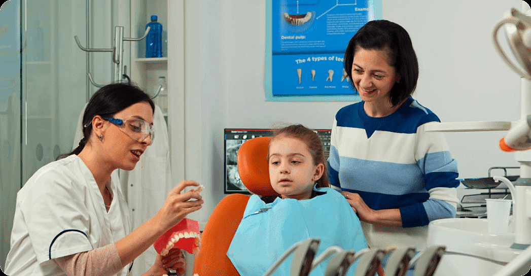 A children's orthodontist shows a dental model to a child in a chair, while an adult stands beside them in the clinic in Suwanee or Tucker, GA