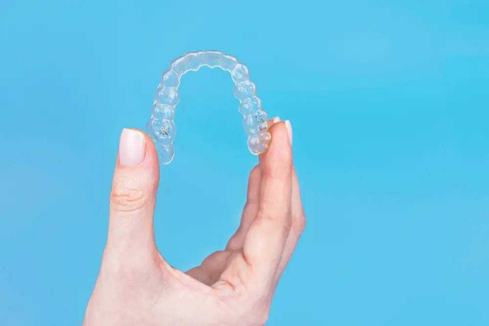 A hand delicately holds a clear dental aligner against a serene blue background, hinting at the promise of a straighter smile. As you admire this innovation, consider exploring Invisalign costs to make your dream smile achievable in Suwanee or Tucker, GA