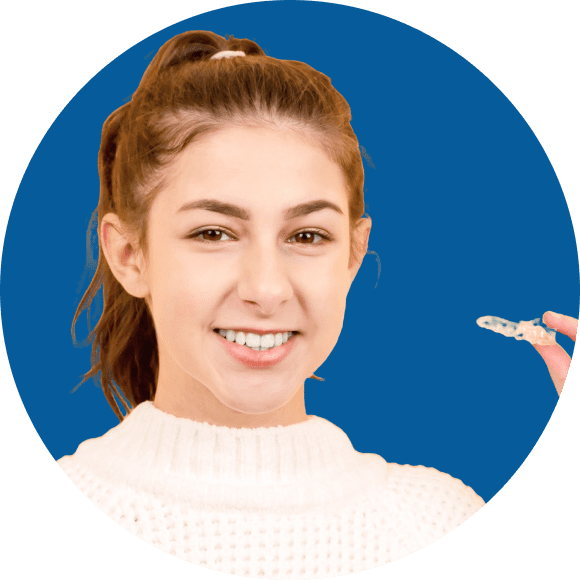 Person smiling and holding an affordable Invisalign dental aligner, wearing a white sweater against a blue background in Suwanee or Tucker, GA