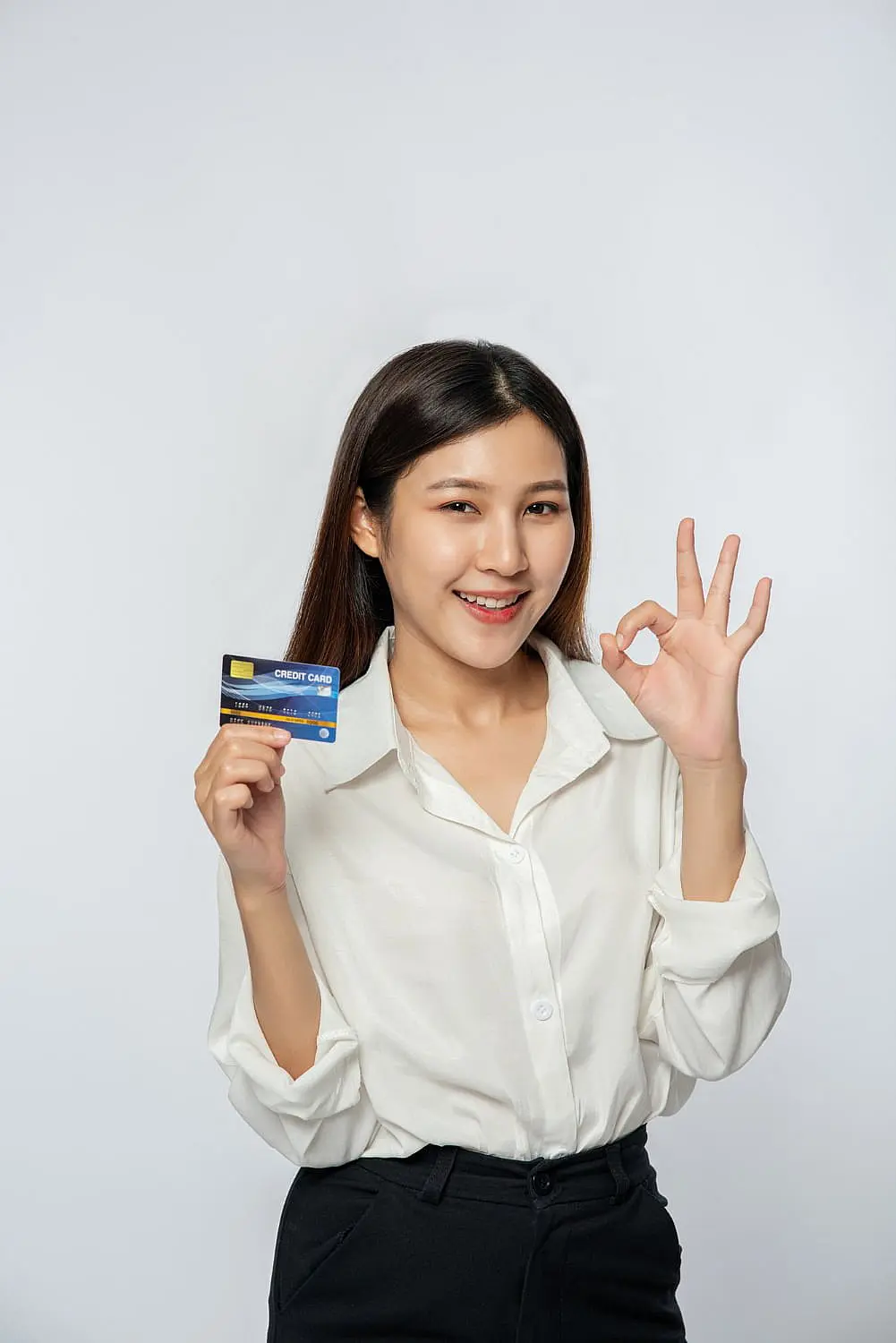 Person in a white shirt holding a credit card and making an "OK" gesture against a plain background, showcasing confidence in an easy braces payment plan in Suwanee or Tucker, GA