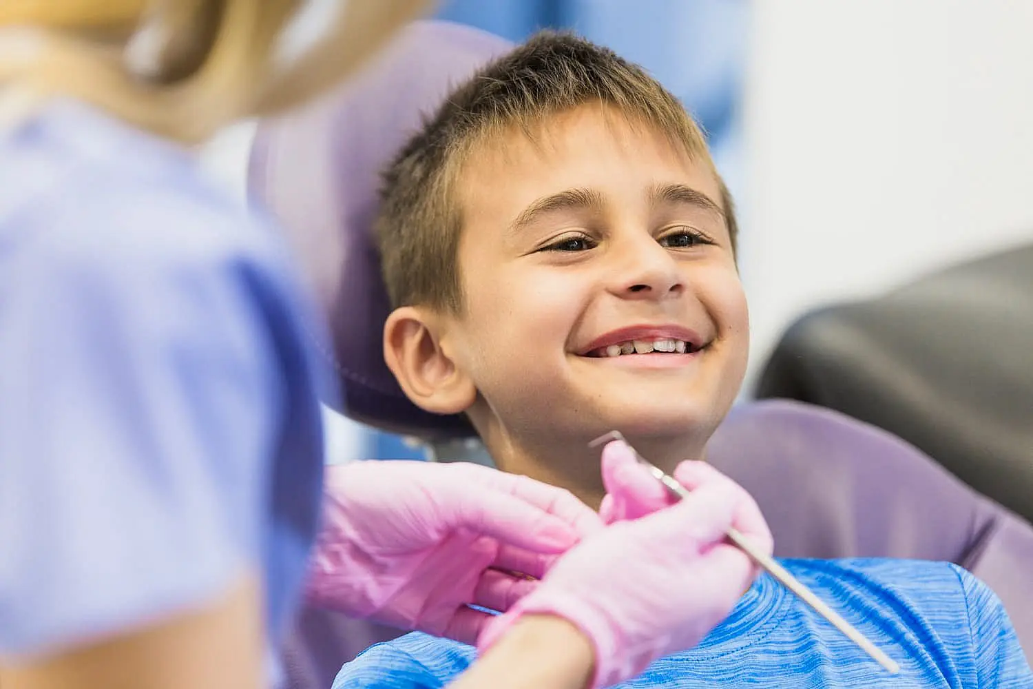 A young boy in a dental chair smiles while a dental professional, wearing pink gloves, prepares to clean his teeth and discuss his new palate expander in Suwanee or Tucker, GA