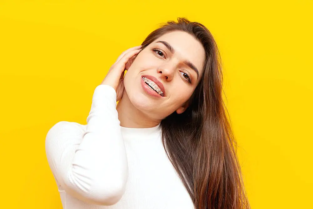 A smiling person showcases their clear braces while wearing a white shirt against a bright yellow background, highlighting the confidence brought by adult orthodontics in Suwanee or Tucker, GA