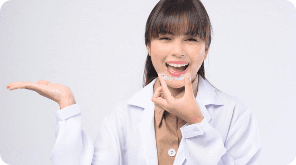 A person in a lab coat is smiling warmly, holding a dental aligner confidently, knowing that orthodontic insurance makes achieving the perfect smile more accessible than ever in Suwanee or Tucker, GA