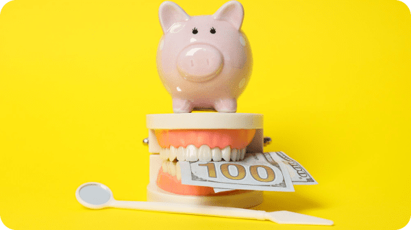 A pink piggy bank perched on a dental model bites a hundred-dollar bill while showcasing orthodontic insurance potential. A dental mirror and explorer sit confidently in front, set against a vibrant yellow background in Suwanee or Tucker, GA