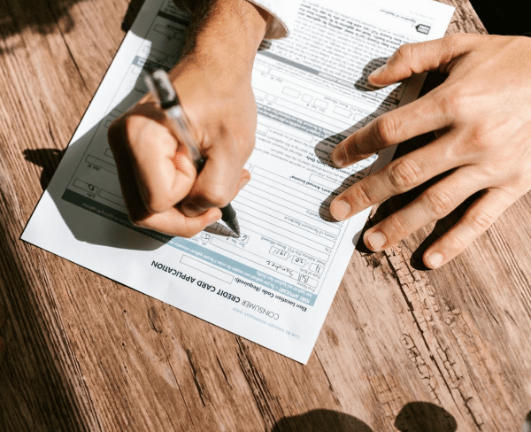 A person is thoughtfully filling out a form on a wooden table, likely pondering whether Invisalign might be covered by insurance in Suwanee or Tucker, GA