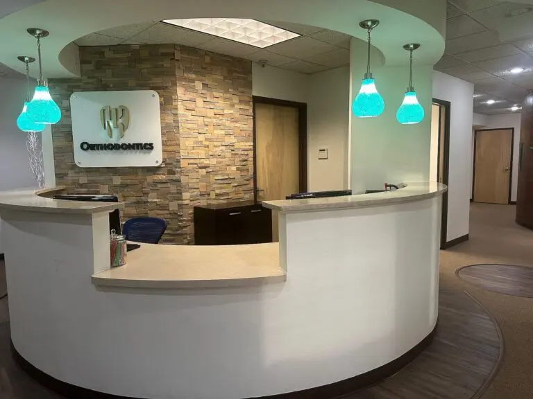 The NK Orthodontics Tucker office welcomes you with a curved white desk, a stone accent wall, and three elegant blue pendant lights in Tucker, GA