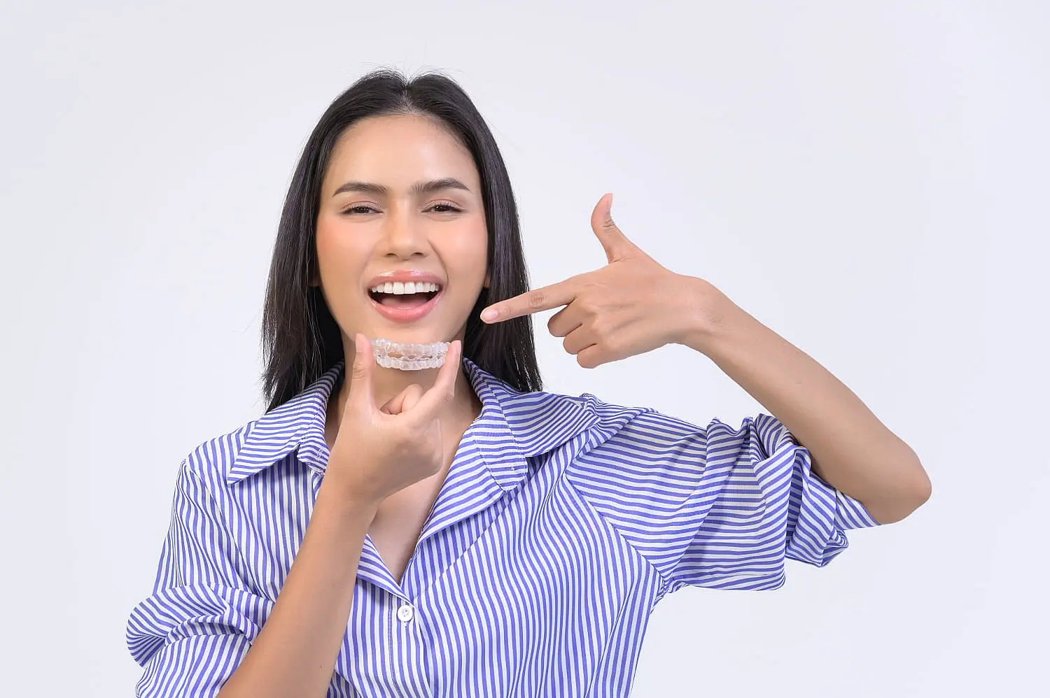 A person in a striped shirt beams with pride while pointing at an Invisalign aligner they're holding, happy that their Invisalign insurance has made achieving a perfect smile easier than ever in Suwanee or Tucker, GA