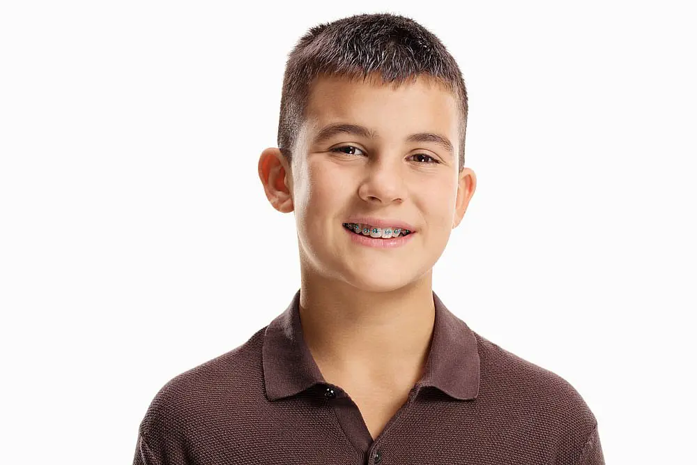 A smiling boy with short hair and affordable braces, wearing a brown polo shirt, stands against a plain white background in Suwanee or Tucker, GA