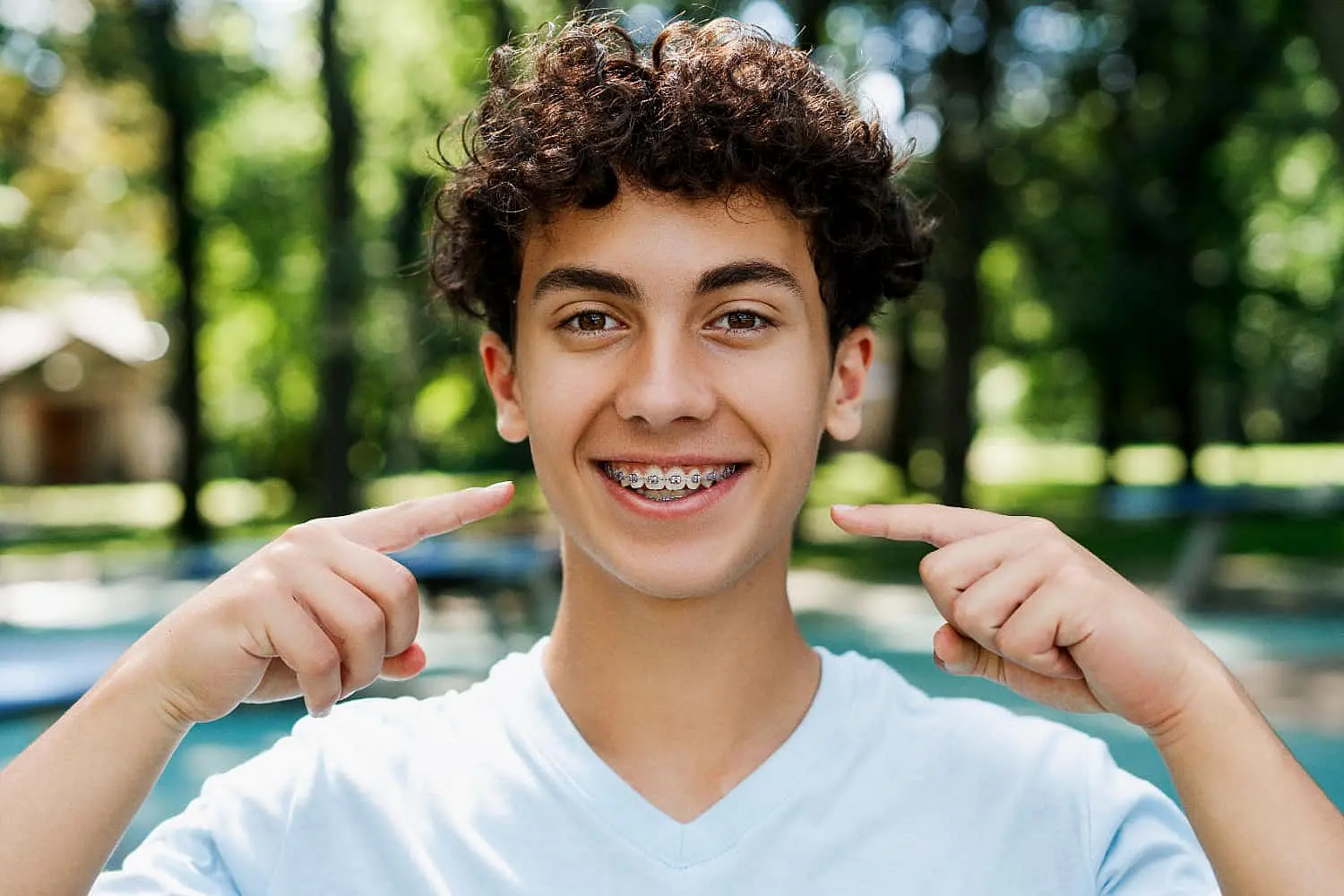 A teen with curly hair beams outdoors, proudly pointing at their affordable braces in Suwanee or Tucker, GA
