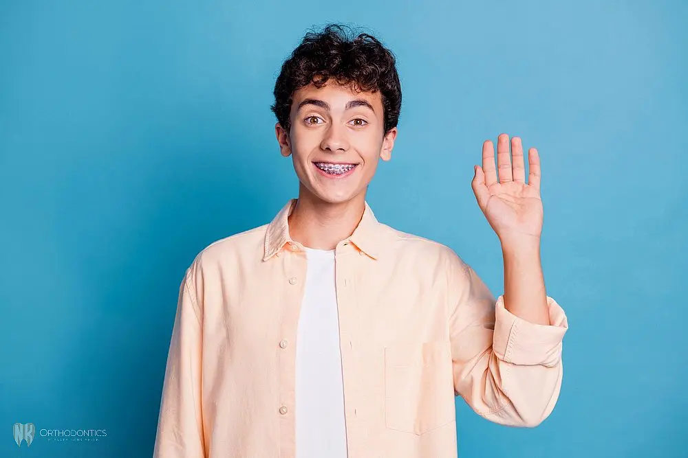 a boy with metal braces waving at the camera after understanding about how long do braces take in suwanee and tucker, ga