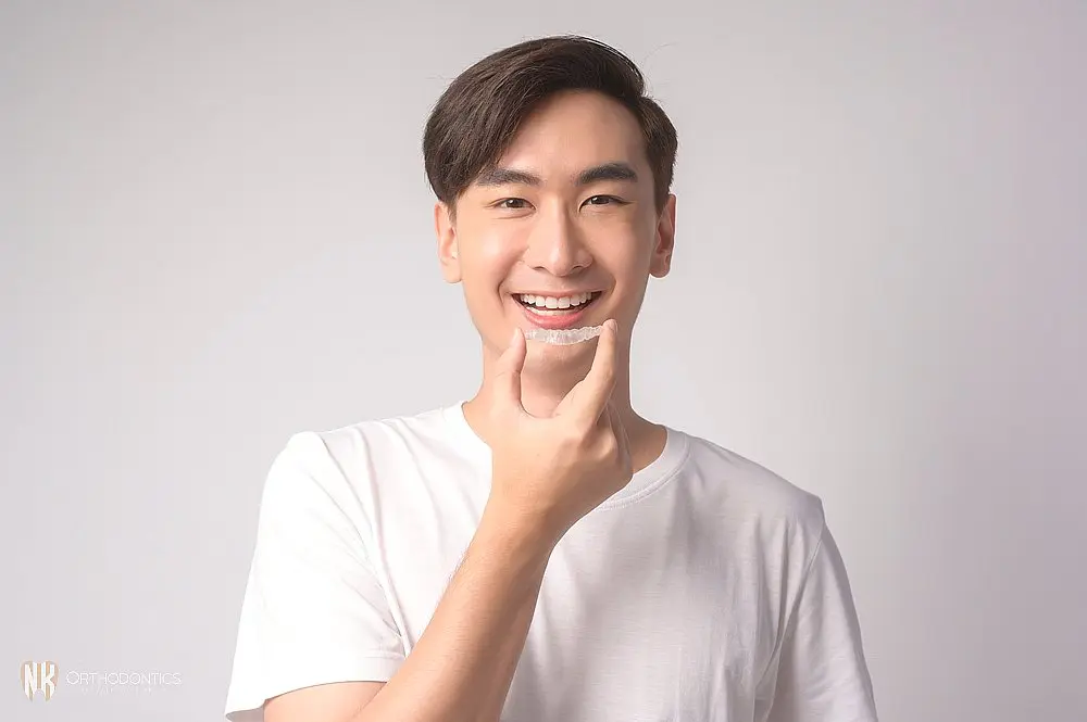 Young man smiling while placing a clear aligner on his teeth, showcasing orthodontic treatment with Invisalign after understanding Does Insurance Cover Invisalign in Suwanee, Tucker, and Cumming, GA.