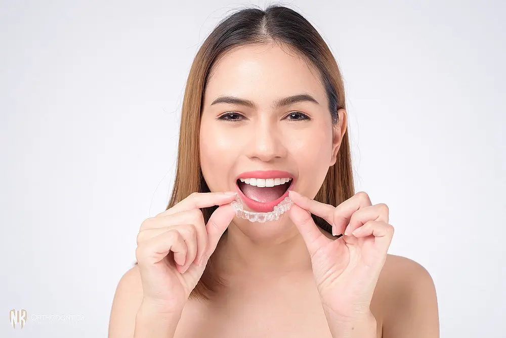 Smiling woman inserting a clear aligner, demonstrating proper use of Invisalign trays after understanding Does Insurance Cover Invisalign in Suwanee, Tucker, and Cumming, GA.