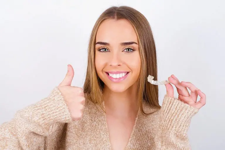 A woman holding a clear dental aligner in one hand and giving a thumbs up with the other after understanding about Does Insurance Cover Invisalign in Suwanee, Tucker, and Cumming, GA