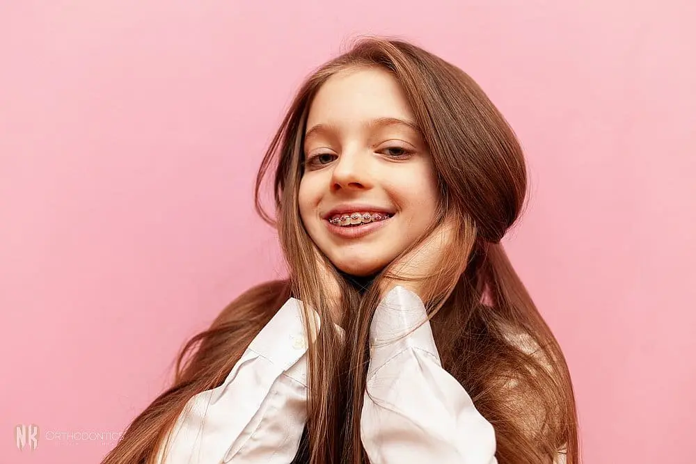 Confident young woman posing against a pink background, smiling naturally after orthodontic braces for overbite in suwanee and tucker, ga.