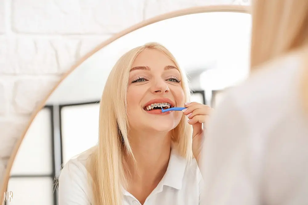 young woman metal braces toothbrush home - How to Floss with Braces in Suwanee and Tucker, GA. 