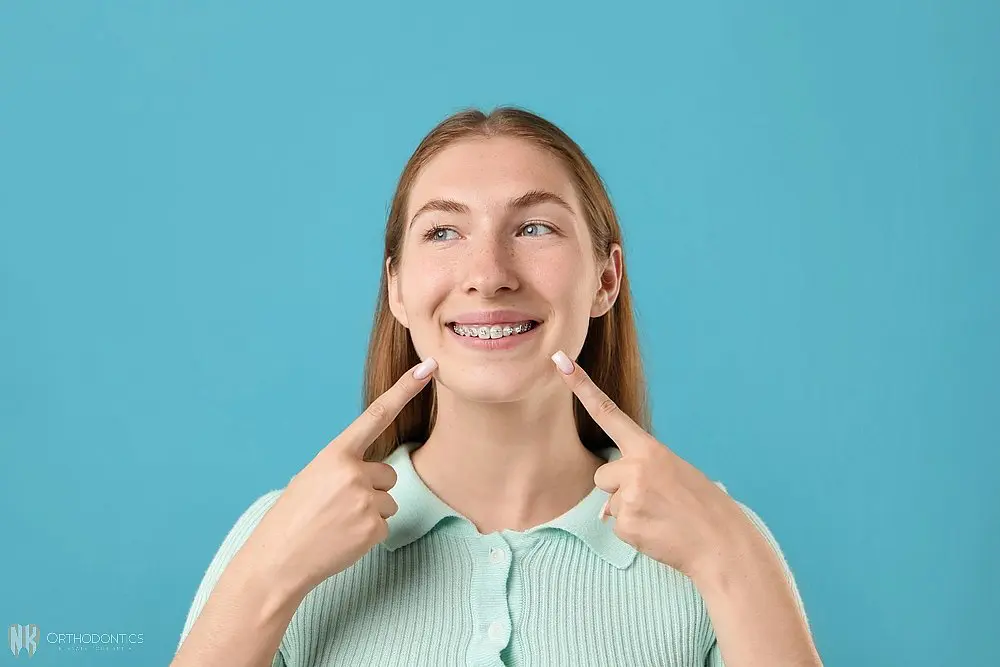 girl pointing her metal braces light blue background - Clear Braces vs Metal Braces in Suwanee and Tucker, GA 