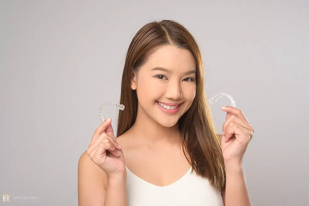 young smiling woman holding invisalign clear aligners white background studio dental - How Long Does Invisalign Take in Suwanee and Tucker, GA 